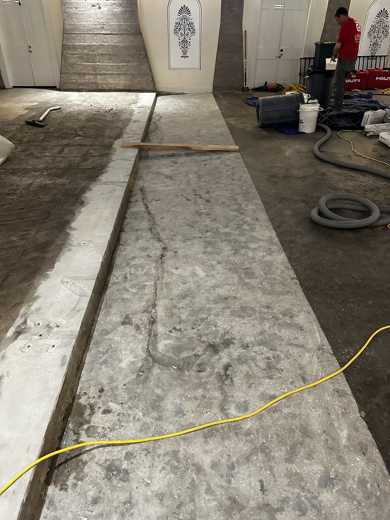 Concrete Repair Services Jacksonville, FL | Con Cure USA IMG 3153 A concrete floor undergoing renovation, with tools and equipment scattered around and stairs leading to a decorated wall in the background.