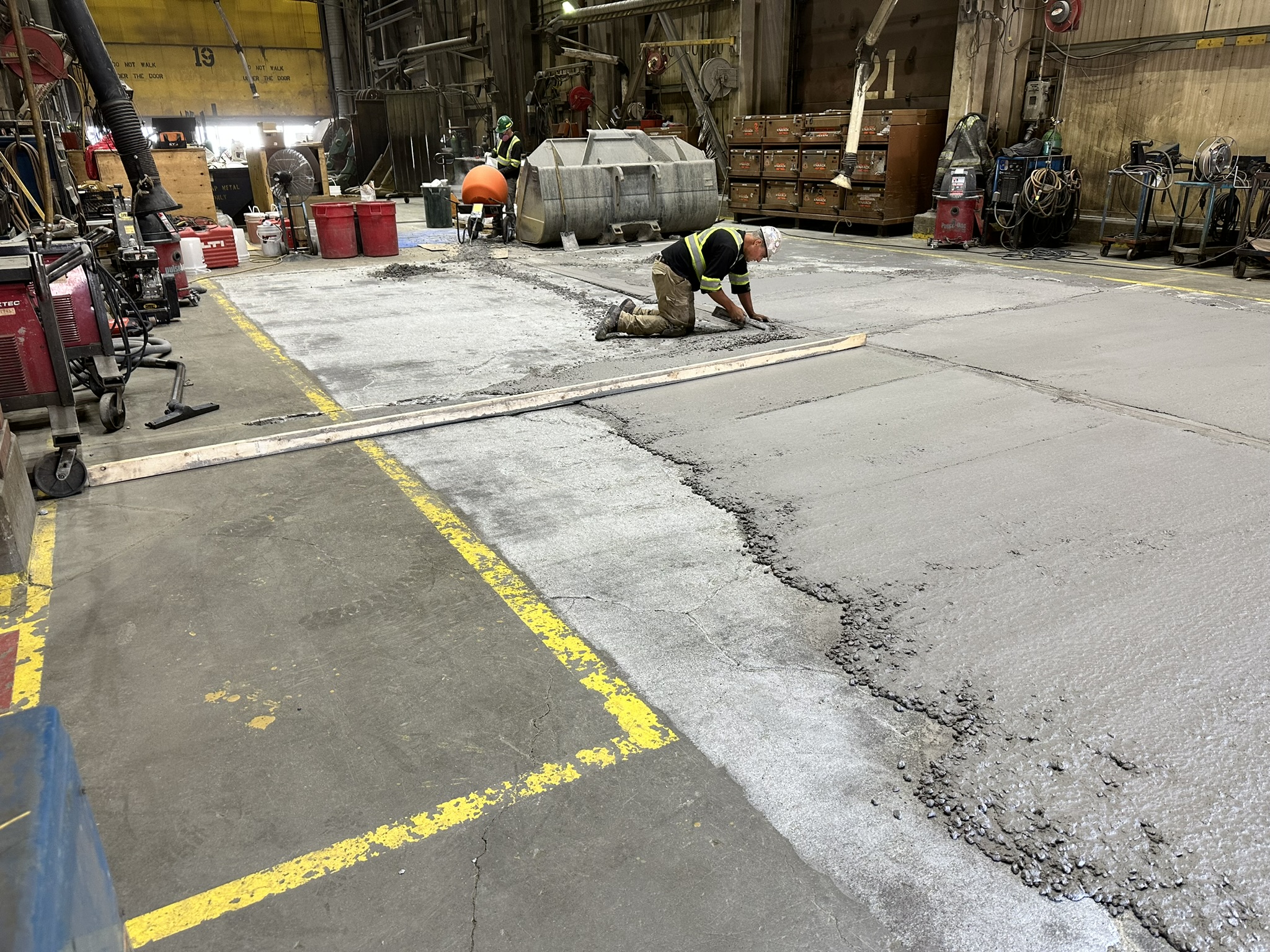 Concrete Repair Services Jacksonville, FL | Con Cure USA IMG 6009 A worker in reflective gear smooths newly poured concrete in a large industrial space, surrounded by tools and materials.