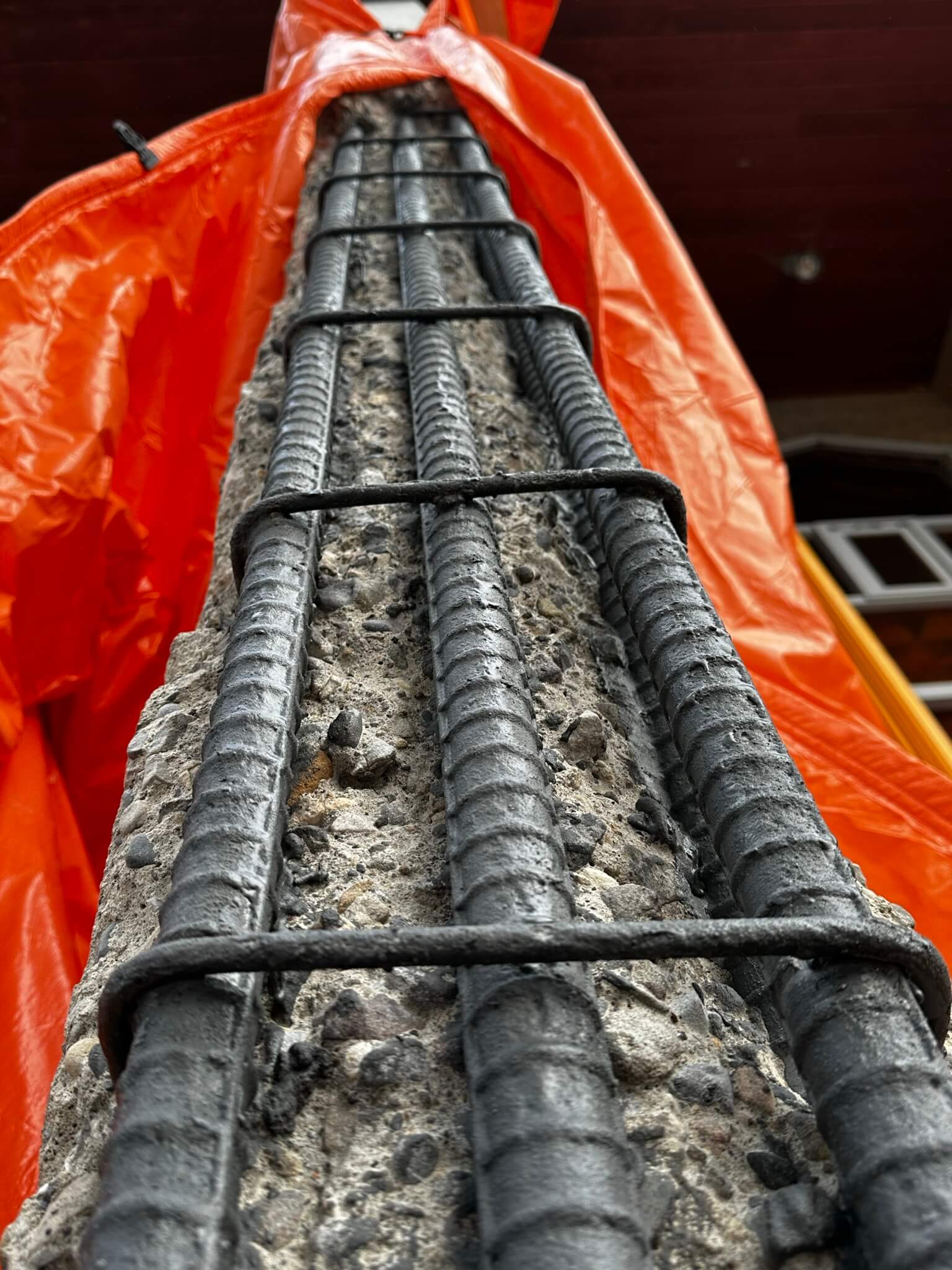 Concrete beam with metal rods covered by an orange tarp, showcasing Con Cure Restoration's work.